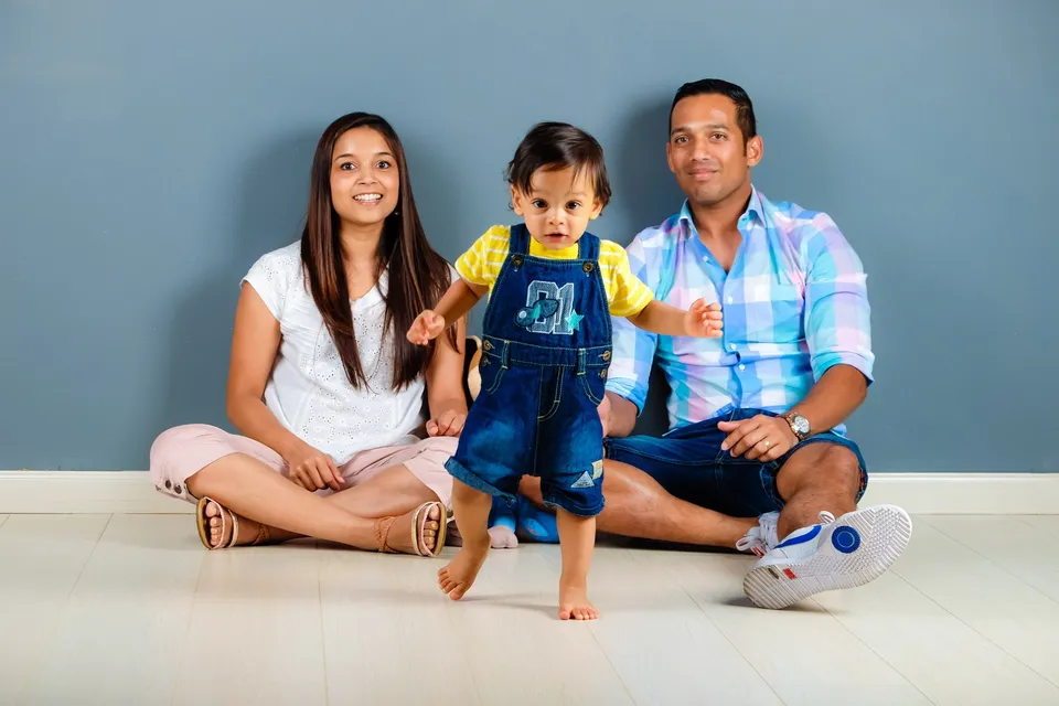 Una familia sentada en el piso mientras un niño pequeño está de pie al frente.